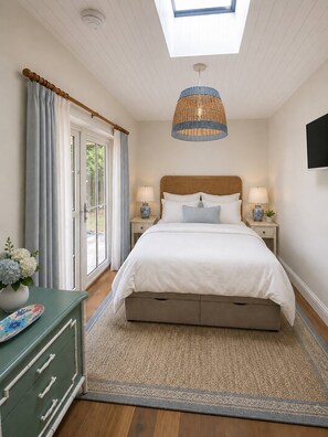 A bedroom with a large bed, two bedside tables with lamps, a green dresser, a large window with curtains, and a ceiling light fixture. - New Stunning House St Ives With Parking (St Ives)