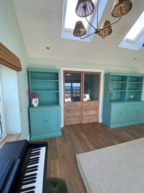 A room with a piano, teal shelving units, a wooden door, and a skylight. - New Stunning House St Ives With Parking (St Ives)