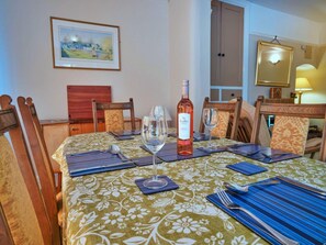 A dining table set with a wine bottle, glasses, and cutlery, surrounded by wooden chairs with cushioned seats. - Charming Art Cottage for 5 (Chesterfield)
