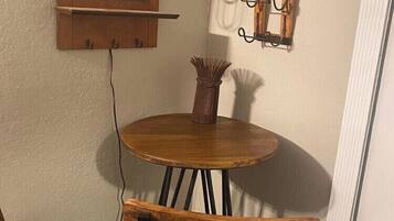 A small dining area with a round wooden table and two chairs, a wall-mounted light fixture, and a mirror with a wooden frame.