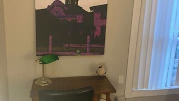 A room with a desk, chair, lamp, and a large painting on the wall.