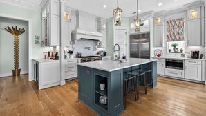 Une cuisine moderne avec des meubles blancs, un îlot central, des luminaires suspendus et des appareils en acier inoxydable.