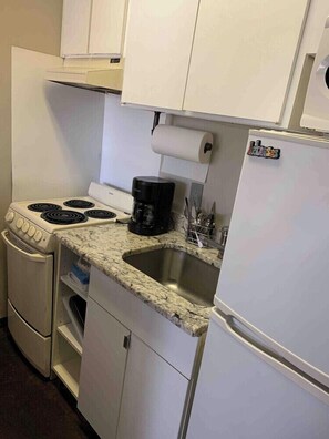 Eine kleine Küchenzeile mit Herd, Kaffeemaschine, Spüle und Kühlschrank.