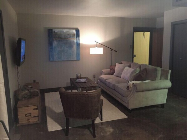 Ein Wohnzimmer mit einer Couch, einem Sessel, einem Couchtisch, einem Gemälde an der Wand und einem Fernseher.