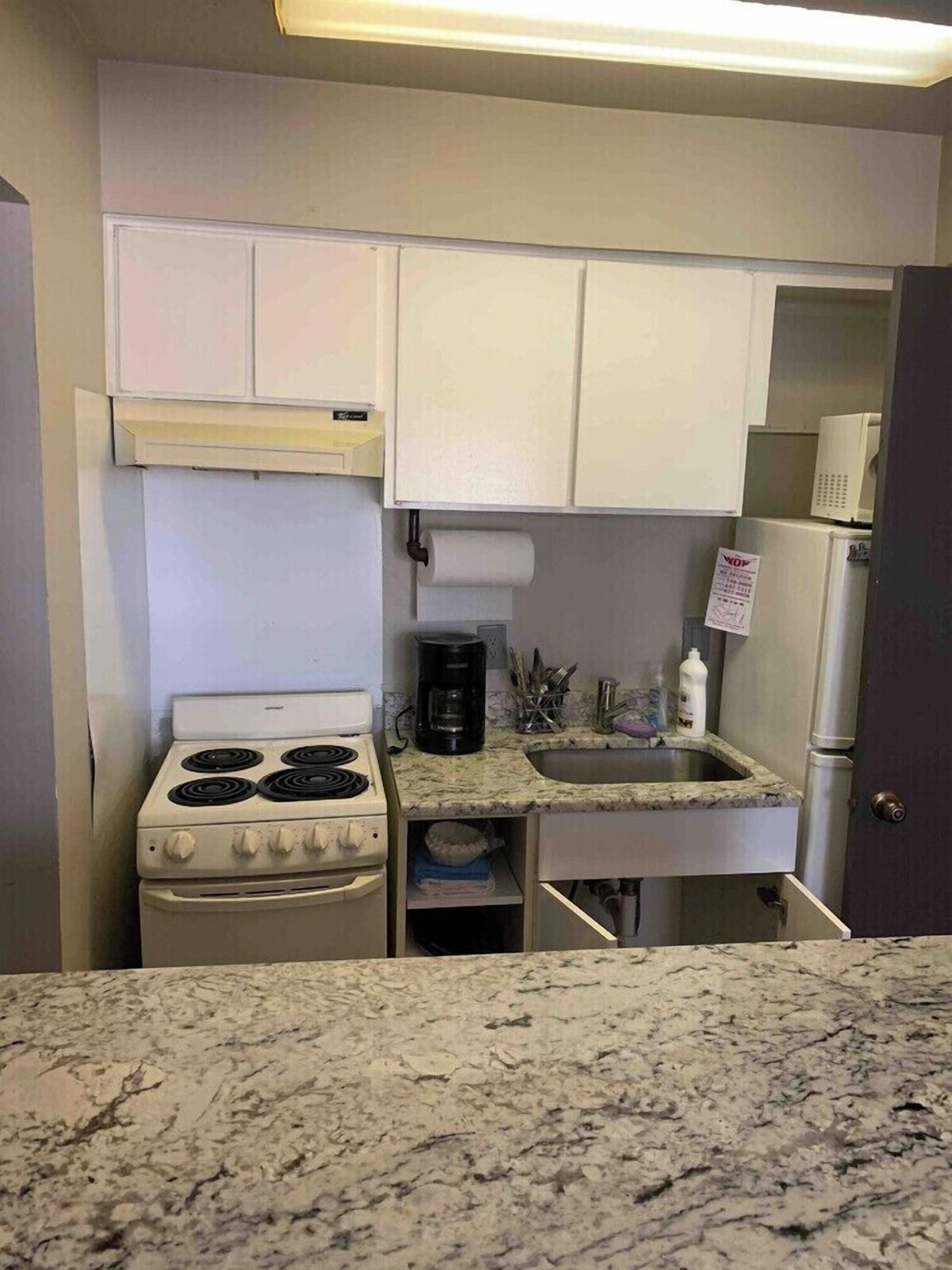A compact kitchen with a white stove, a sink, and cabinets.