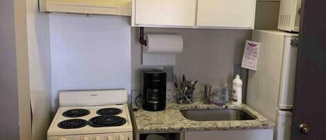A compact kitchen with a white stove, a sink, and cabinets.