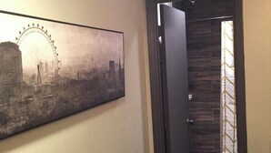 Un couloir orné d’un tableau représentant un paysage urbain, avec une porte en bois et un rideau à motifs.