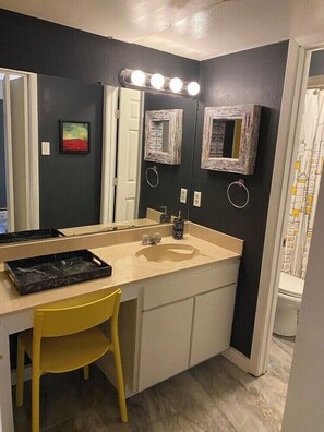 A bathroom with a vanity, mirror, and a yellow chair. - 2720 #104 Oaklawn furnished rental (Dallas)