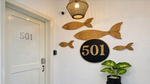 Ovi, jonka numerona on 501, seinä, jossa on puisia kalakoristeita, pyöreä kyltti, jossa on numero 501, ja ruukussa oleva kasvi.