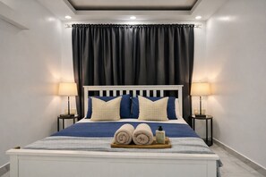 A bedroom with a bed, two bedside lamps, a headboard, and a tray with towels and a bottle. - Lovely 2-Bedroom Beach Apartment with Pool #2 (Punta Cana)