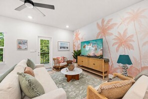A living room with a sofa, a coffee table, a television on a wooden cabinet, and a wall with a palm tree pattern. - Palm Paradise *Minutes to Beach* (SANTA RSA BCH)