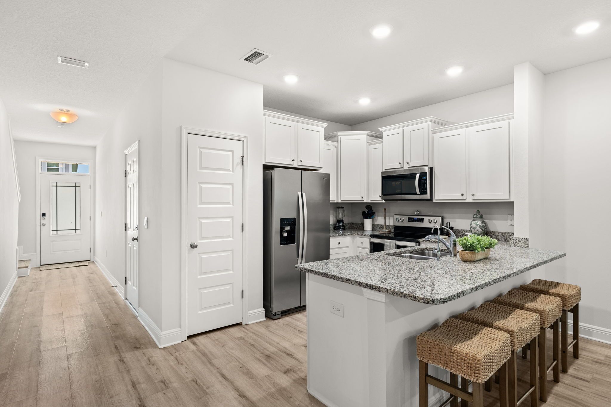 A modern kitchen with white cabinetry, stainless steel appliances, and a granite countertop island with bar stools.