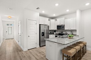 A modern kitchen with white cabinetry, stainless steel appliances, and a granite countertop island with bar stools. - Palm Paradise *Minutes to Beach* (SANTA RSA BCH)