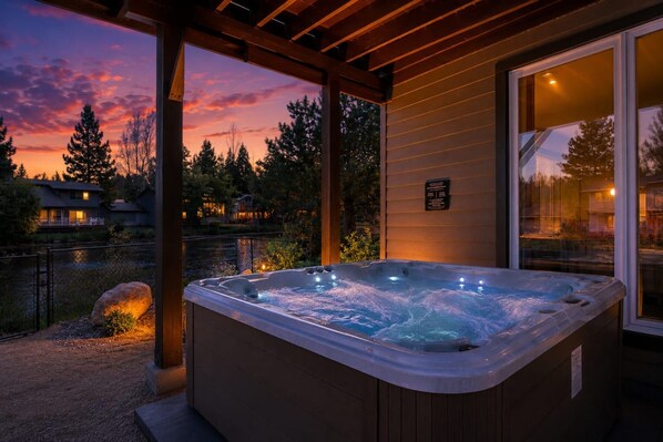 A hot tub in a covered outdoor area with a view of a sunset and a lake.