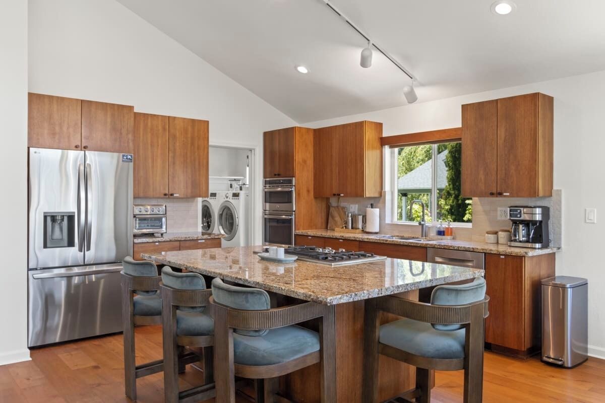 Una cocina moderna con electrodomésticos de acero inoxidable, armarios de madera, encimera de granito y taburetes de bar.