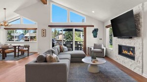 Un amplio salón con sofá seccional, chimenea, televisor de pantalla plana y ventanas grandes.