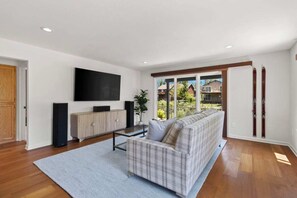 Un salon moderne avec un canapé, un téléviseur, des haut-parleurs et une fenêtre donnant sur un beau paysage.