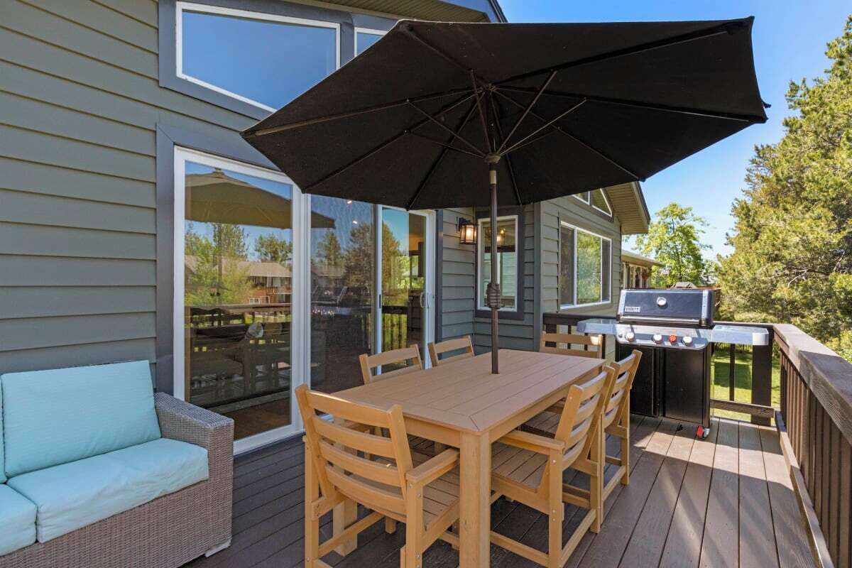 Una terrazza con tavolo e sedie di legno, un barbecue e un grande ombrellone.