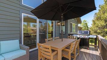 Una terrazza con tavolo e sedie di legno, un barbecue e un grande ombrellone.