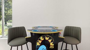 Una habitación con una mesa, dos sillas, un ventanal con persianas y vistas a zonas verdes.