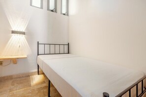 A small, single-bed room with a metal frame, a white mattress, and a wall-mounted light fixture. - Oceanfront condo with a pool, hot tub, and spectacular view (Acapulco de Juárez)