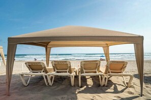A beach umbrella with two lounge chairs under it, a sandy beach, and the ocean in the background. - Oceanfront condo with a pool, hot tub, and spectacular view (Acapulco de Juárez)