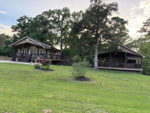 A two-story lodge with a porch, a small garden, and a large tree in front. - Lakeside Living w/ Separate Bar, Hot Tub, Firepit (Point Blank)