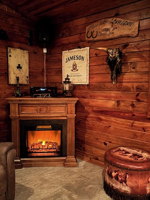 A cozy room with a fireplace, wooden walls, a sign reading 'Live like someone left the gate open,' and a mounted animal head. - Lakeside Living w/ Separate Bar, Hot Tub, Firepit (Point Blank)