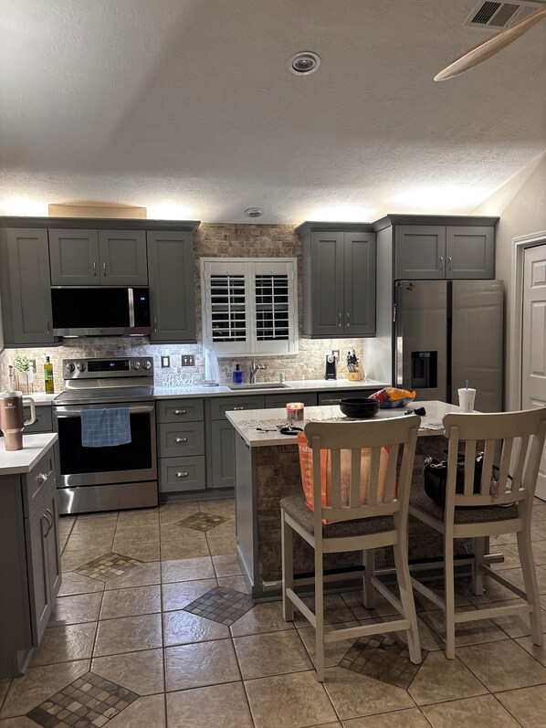 A kitchen with grey cabinets, a stainless steel refrigerator, a microwave, and an oven. - Lakeside Living w/ Separate Bar, Hot Tub, Firepit (Point Blank)