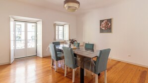 A dining area with a glass table, four chairs, a pendant light, and a painting on the wall. - Sunny Príncipe Real Villa · Patio · 4BR for 12 (Lisboa)