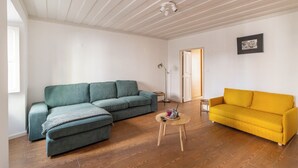 A living room with a green sectional sofa, a yellow sofa, a small round table with a remote control, and a floor lamp. - Sunny Príncipe Real Villa · Patio · 4BR for 12 (Lisboa)