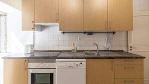 A kitchen with wooden cabinets, a dishwasher, an oven, a sink, and a window. - Sunny Príncipe Real Villa · Patio · 4BR for 12 (Lisboa)