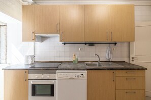 Eine Küche mit Holzschränken, einem Geschirrspüler, einem Backofen, einer Spüle und einem Fenster.