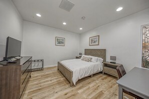 Un dormitorio con cama, mesitas de noche, un escritorio, televisor y obras de arte en las paredes.