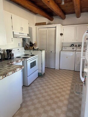 A compact kitchen with white cabinets, a stove, and a washing machine. - Classic Historic Adobe Home on Kit Carson Road in Taos (Taos)