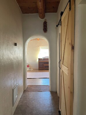A hallway with a wooden door on the right, a white wall on the left, and a wooden ceiling. - Classic Historic Adobe Home on Kit Carson Road in Taos (Taos)