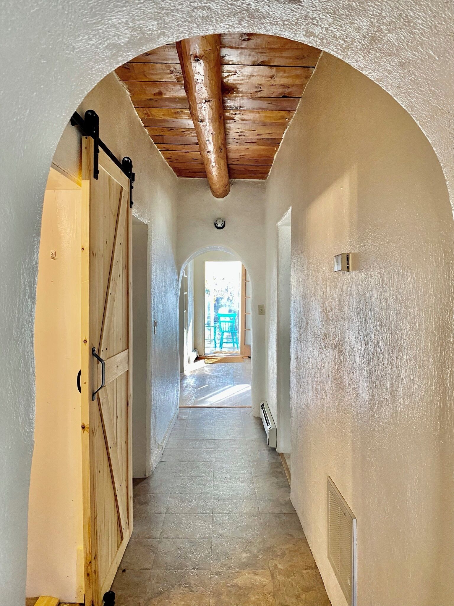 Ein Flur mit einer Holztür, einer Decke mit freiliegenden Balken und Blick in einen Raum mit einem Sessel.