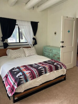 Ein Schlafzimmer mit Bett, einem Fenster mit Vorhängen, einer Tür und einem Schminktisch.
