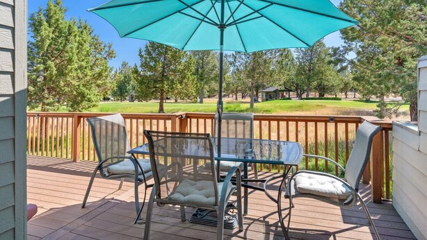 A patio with a table and chairs, a large umbrella, and a view of a grassy area with trees. - Present Pheasant - Cute & Updated, Close to Everything, Golf, Amenities, Perfect For Family (Redmond)