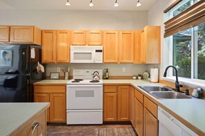 A modern kitchen with wooden cabinets, a stainless steel refrigerator, a microwave, an electric stove, and a sink.