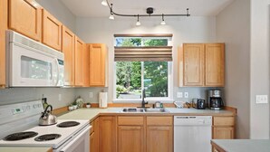 A kitchen with wooden cabinets, a white stove, a dishwasher, a window with blinds, and a coffee maker. - Present Pheasant - Cute & Updated, Close to Everything, Golf, Amenities, Perfect For Family (Redmond)