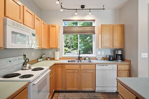 A kitchen with wooden cabinets, a white stove, a dishwasher, a window with blinds, and a coffee maker. - Present Pheasant - Cute & Updated, Close to Everything, Golf, Amenities, Perfect For Family (Redmond)