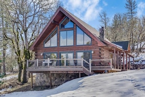A log cabin with a balcony, large windows, and a stone chimney.