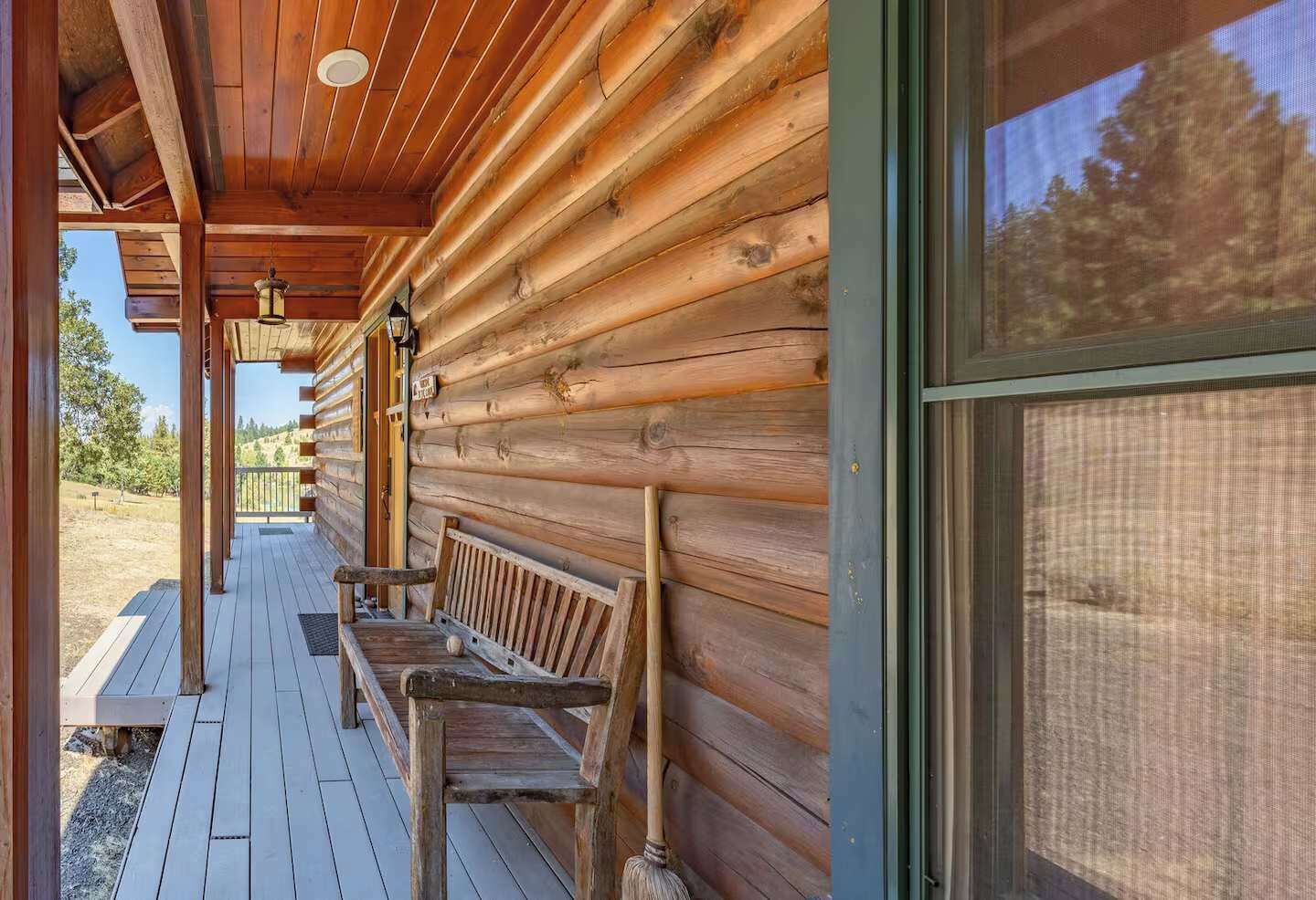 A wooden cabin with a porch, benches, and a large window.