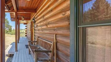 A wooden cabin with a porch, benches, and a large window.