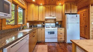 A wooden cabin interior with a kitchen featuring granite countertops, a stove, and a refrigerator. - Straight From The Heart (Lyle)