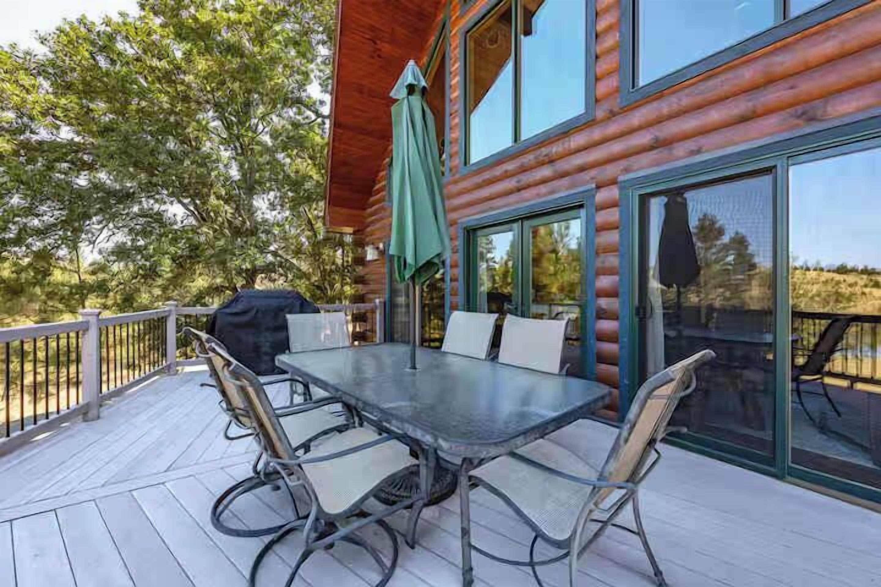 A wooden cabin with a deck, a table with chairs, and a grill.