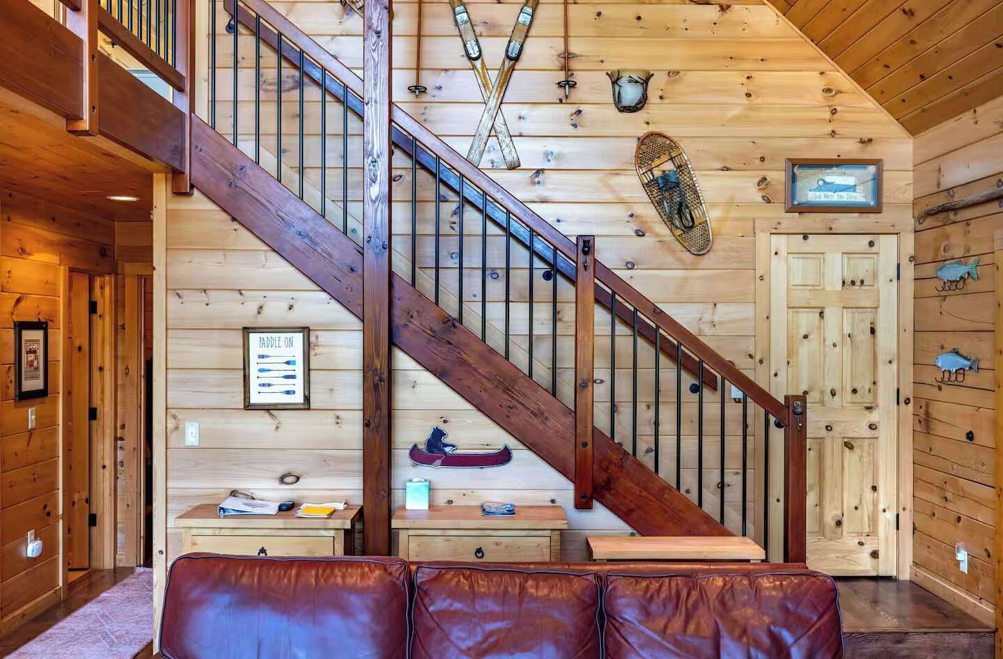 A wooden interior with a staircase, a paddleboard, and a canoe on the wall.