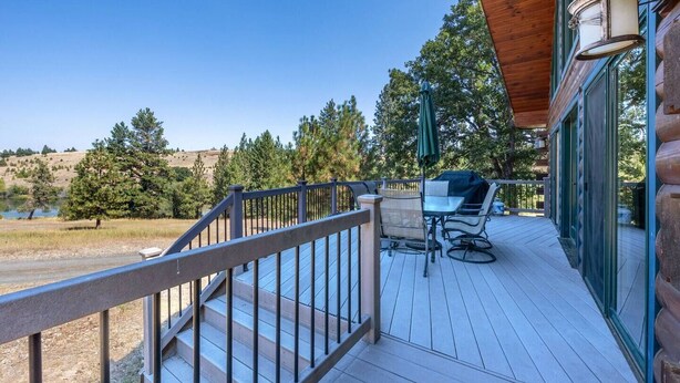 A wooden deck with outdoor furniture, a railing, and a view of a lake and trees. - Straight From The Heart (Lyle)