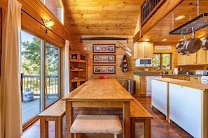 A wooden interior with a central table, shelves with framed pictures, a kitchen area with a microwave, and a sign indicating 'CHERRIES'. - Straight From The Heart (Lyle)